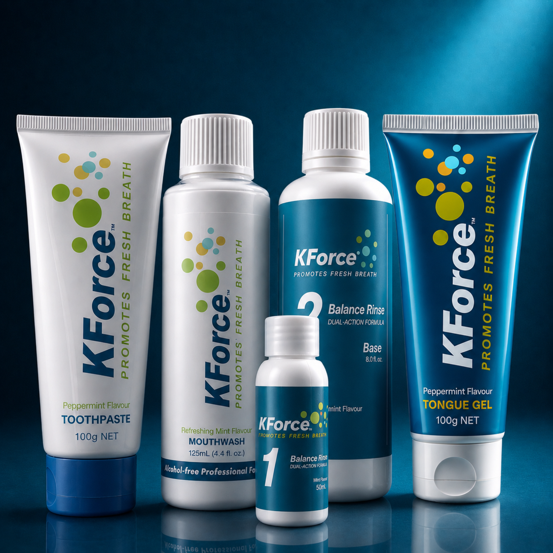A group of KForce oral care products arranged together on a dark blue reflective studio background: a white toothpaste tube, a white mouthwash bottle, a blue balance rinse bottle, a smaller blue tonus gel bottle, and a matching blue toothpaste tube. The products show KForce branding and flavor text including peppermint flavour.