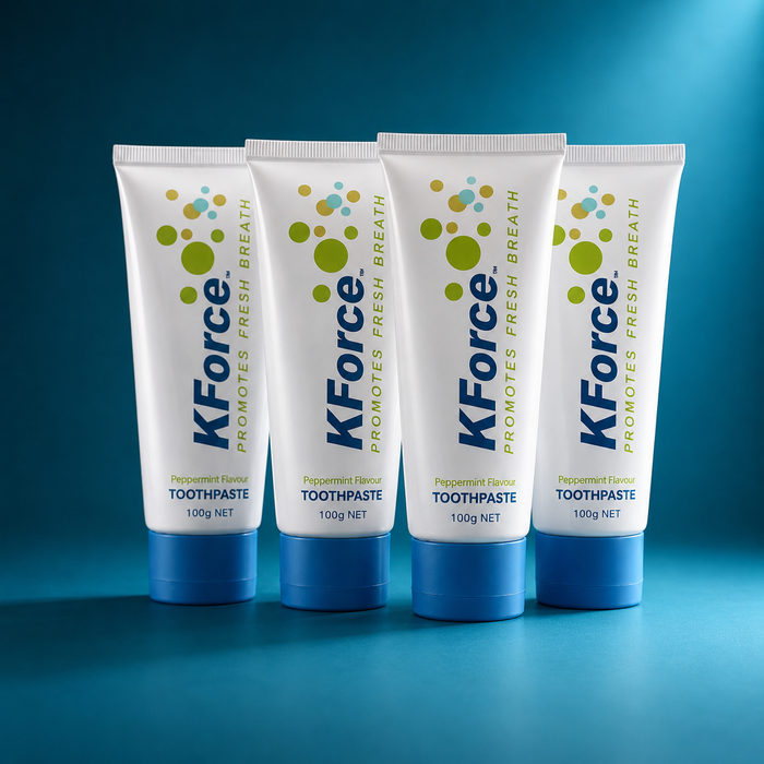 Four tubes of KForce Promotes Fresh Breath toothpaste arranged in a row on a blue gradient background.
